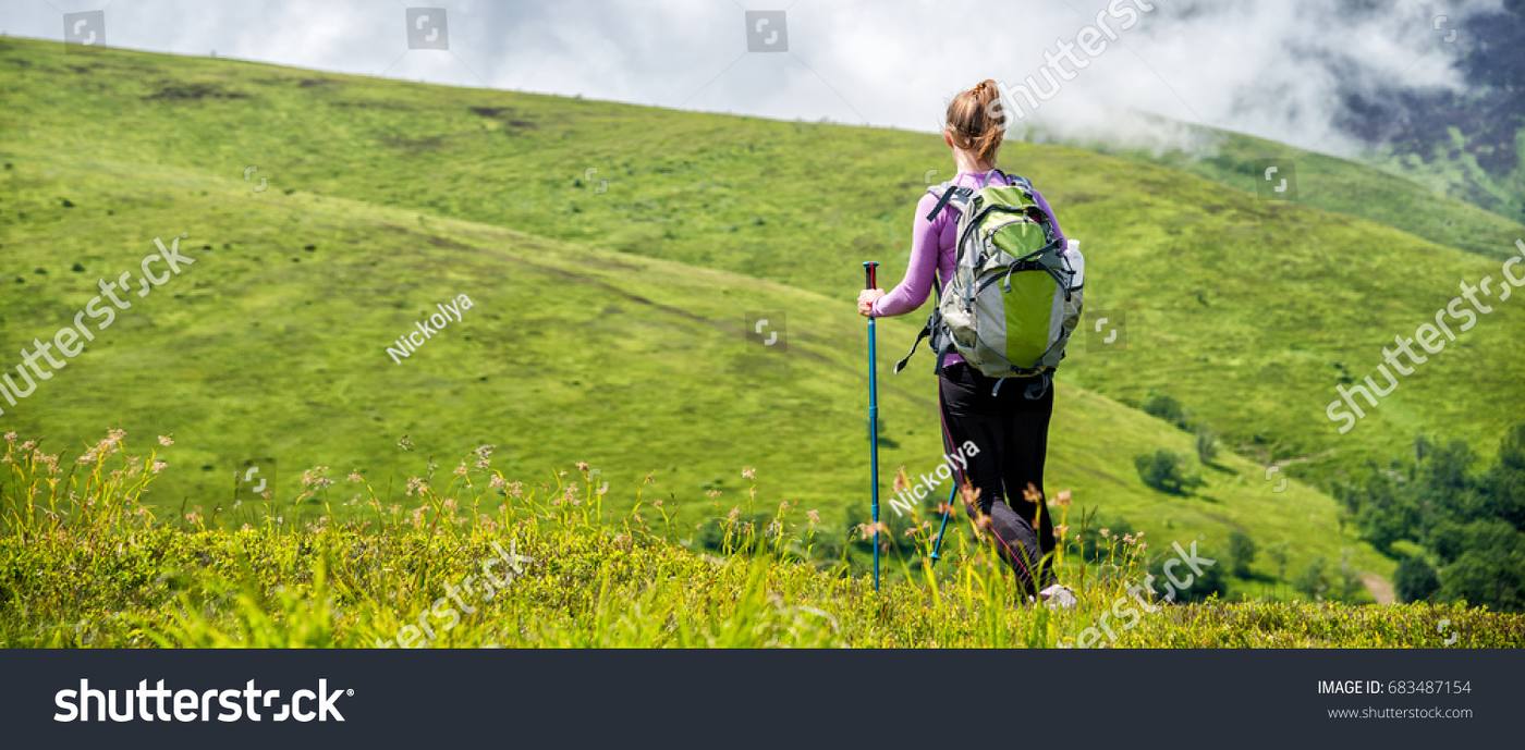 A woman walking uphill on a trail through green California hills