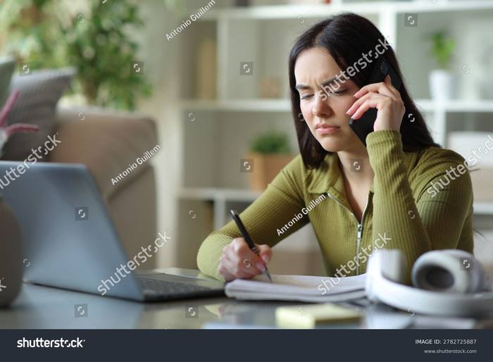 A woman at a desk on the phone, brow furrowed, notes in front of her