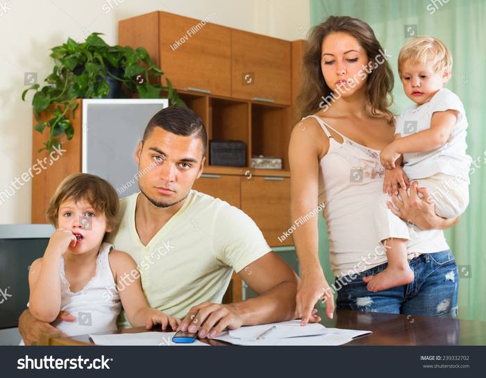Two parents at a table with paperwork while their young children need them