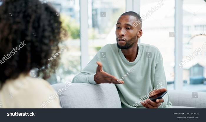 A man on a sofa speaking to a partner whose back is to the camera