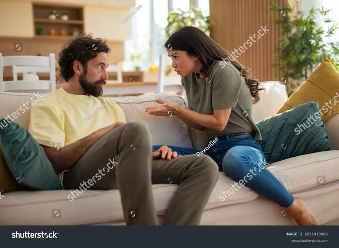 A couple sitting at opposite ends of a sofa, turned toward each other mid-conversation